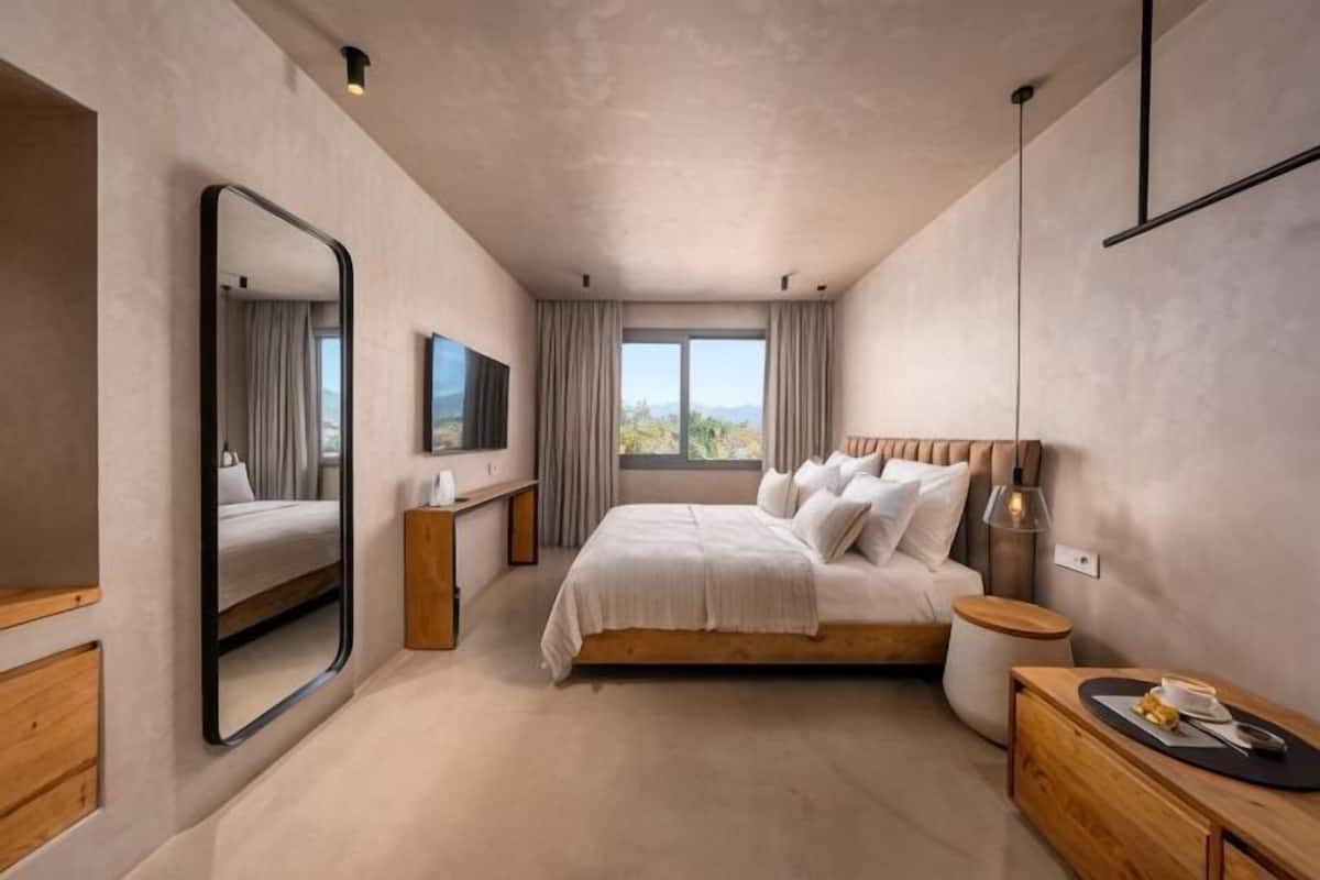 Ein Schlafzimmer mit Bett, Spiegel, Fernseher, Nachttisch, Lampe und einem Fenster mit Vorhängen.