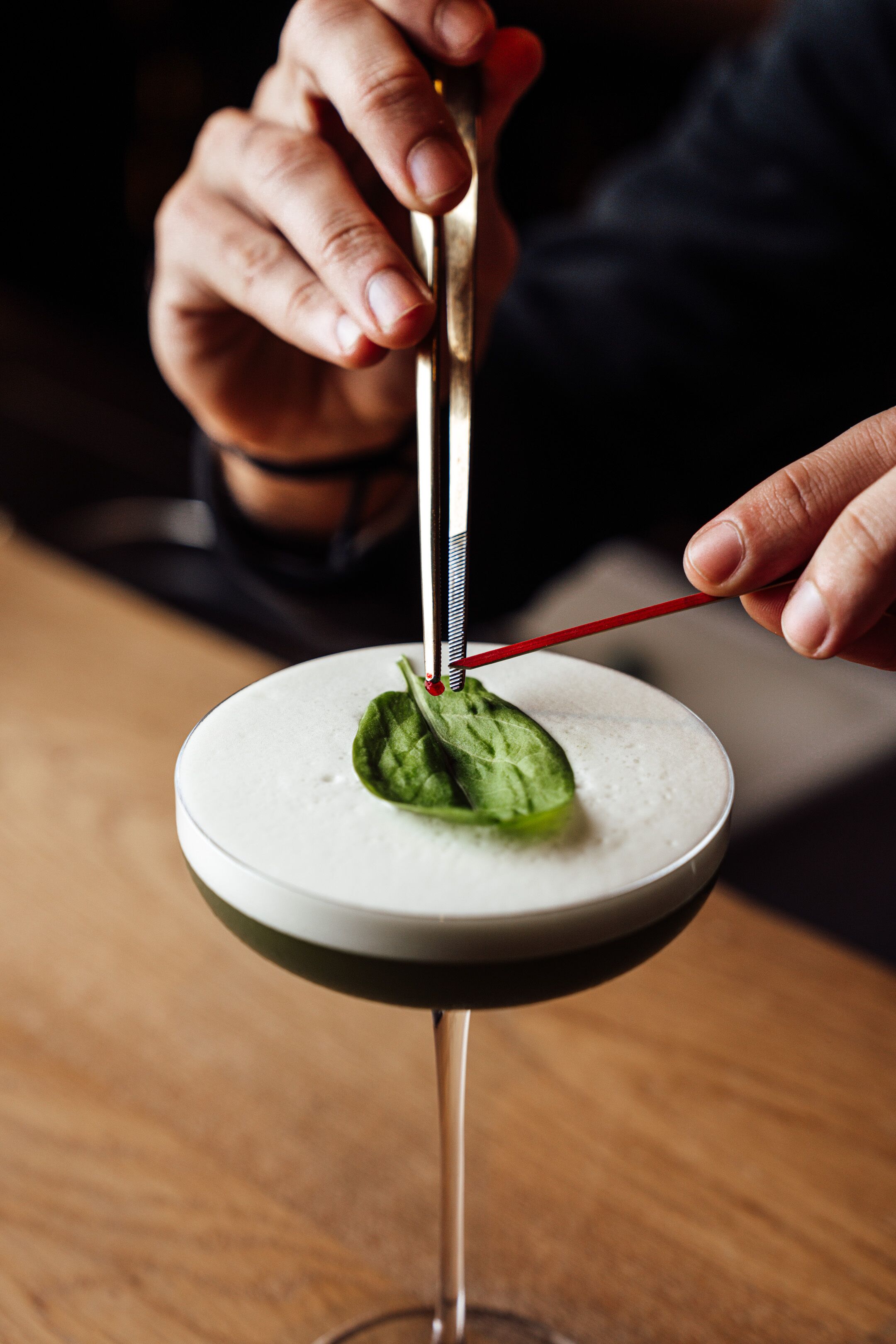 A person using a tool to extract a leaf from a cocktail.