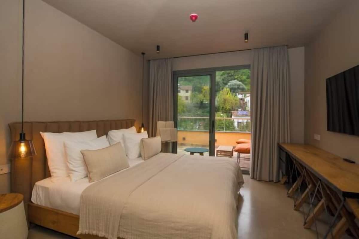 Ein Schlafzimmer mit Bett, Nachttisch, Lampe und Blick ins Freie.