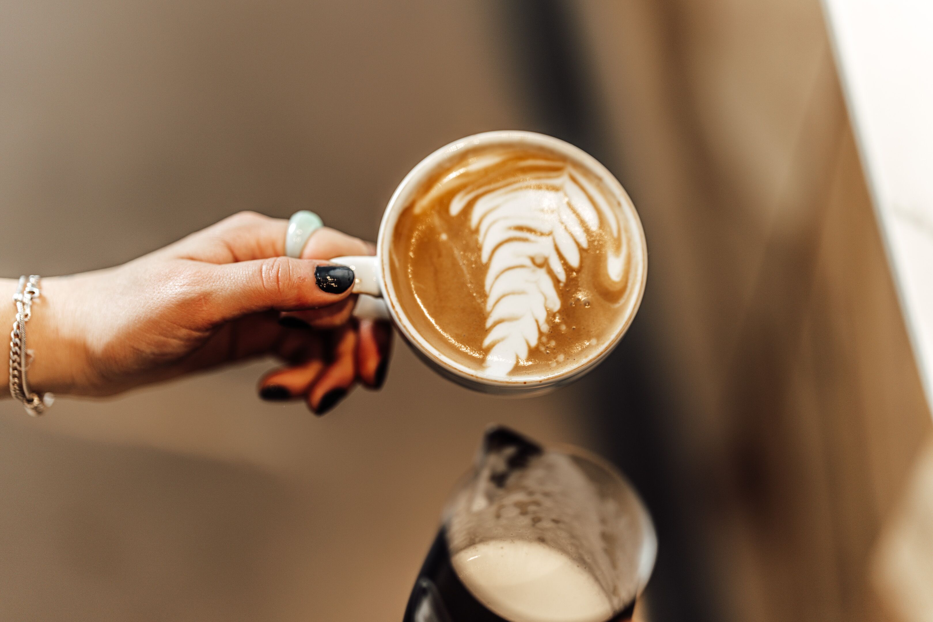 Een hand die een koffiekop vasthoudt met latte art.