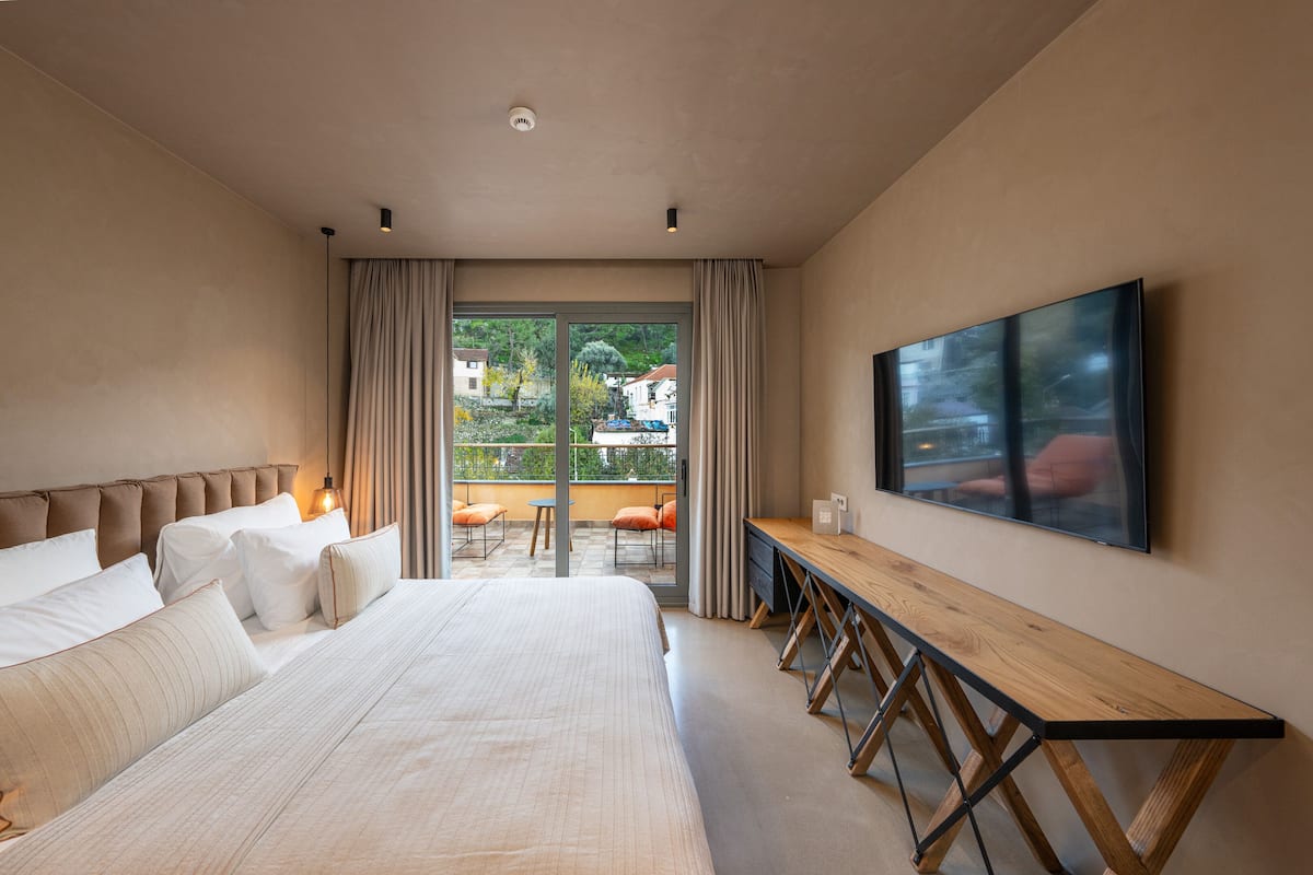 Ein modernes Hotelzimmer mit einem großen Bett, einem Holztisch und einem großen Fenster mit Blick ins Freie.