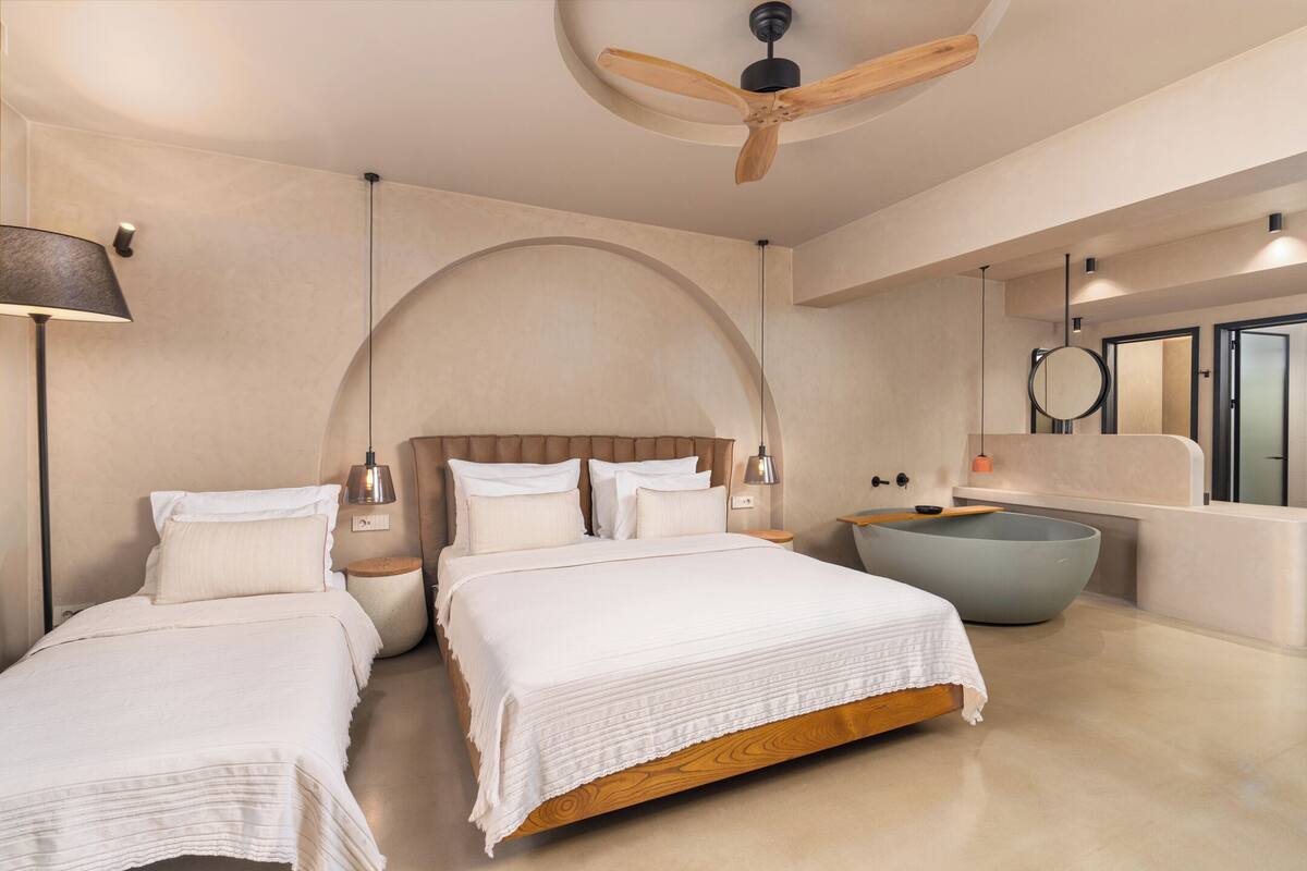 Ein modernes Schlafzimmer mit zwei Betten, einer großen Badewanne und einem Deckenventilator.