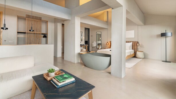 A modern hotel room with a large window, a bathtub, a sofa, and a coffee table with books. - Roome (Fethiye)
