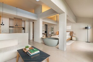 Ett modernt hotellrum med ett stort fönster, ett badkar, en soffa och ett soffbord med böcker.