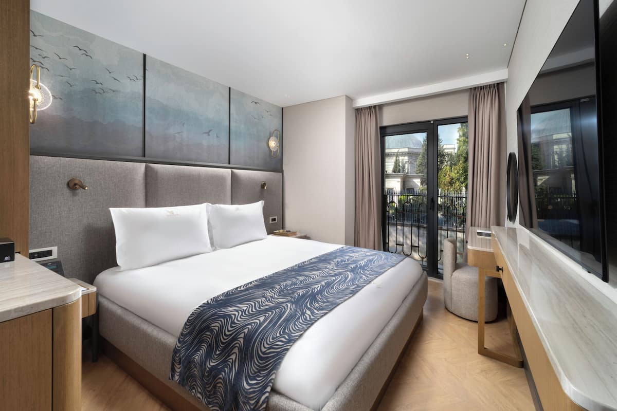 Habitació d'hotel moderna amb un llit gran, una taula de treball i un balcó amb vistes.
