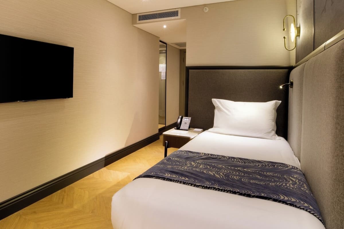 Habitació d'hotel amb llit, taulell de nit i televisió penjada.