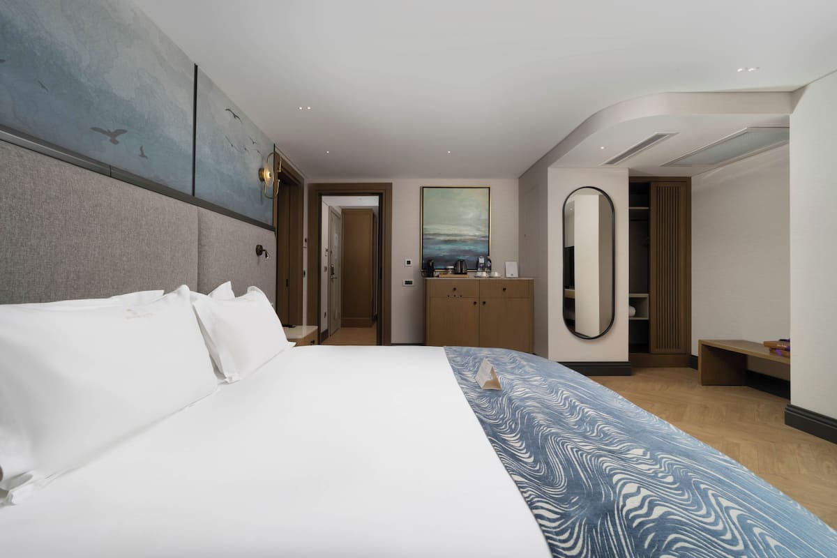 Una habitació d'hotel moderna amb un llit gran, un armari de fusta, un mirall i un quadre a la paret.