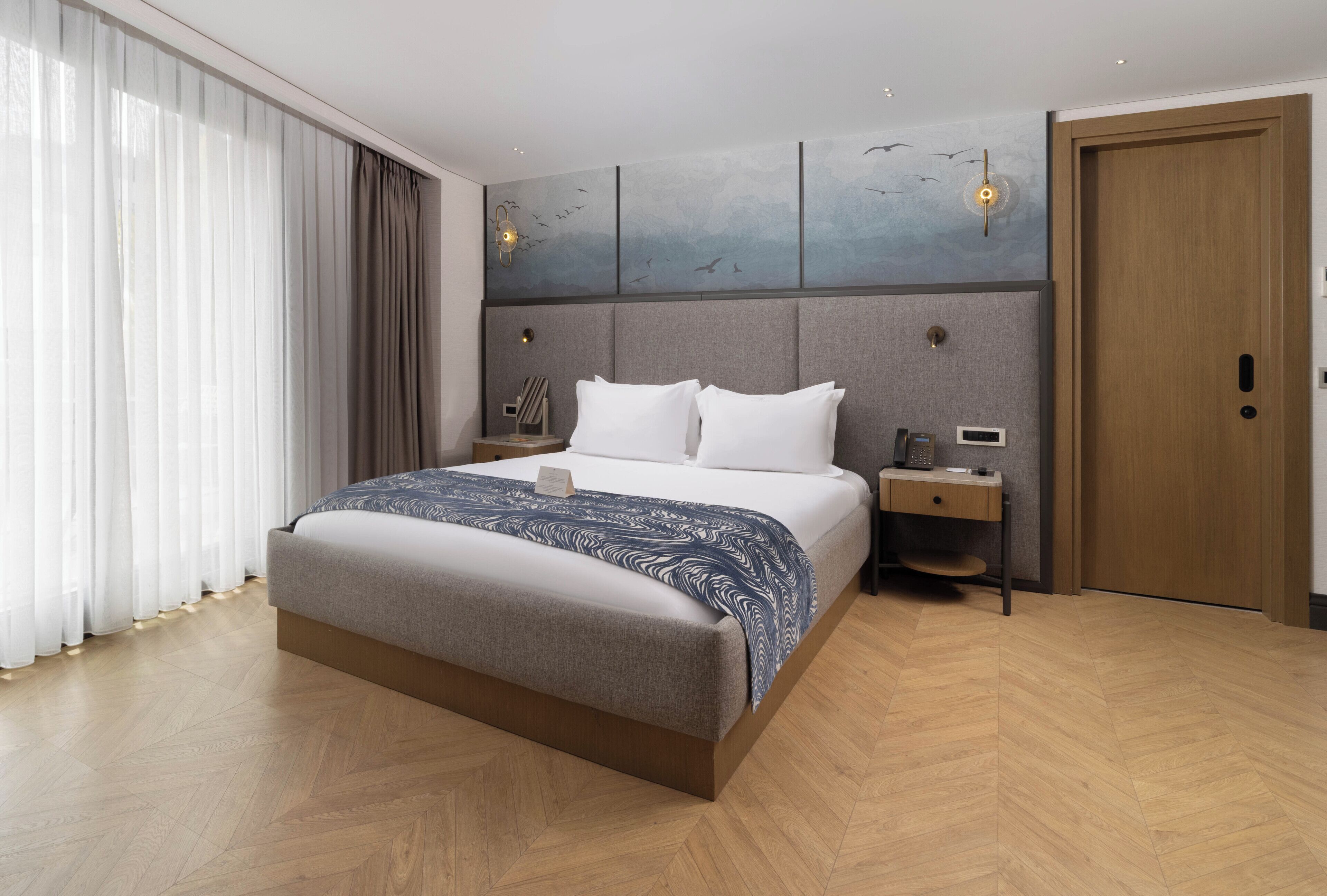 Ein modernes Hotelzimmer mit einem großen Bett, einem Nachttisch, einer Holztür und einer Wand mit Wandgemälde.