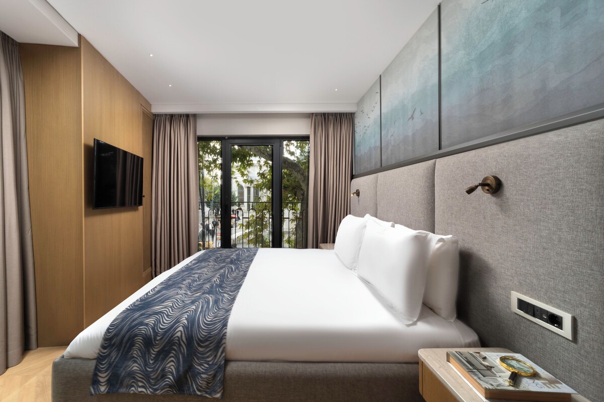 Ein modernes Hotelzimmer mit einem großen Bett, einem Flachbildfernseher, einer Wandpaneele aus Holz und Blick durch eine Glastür.