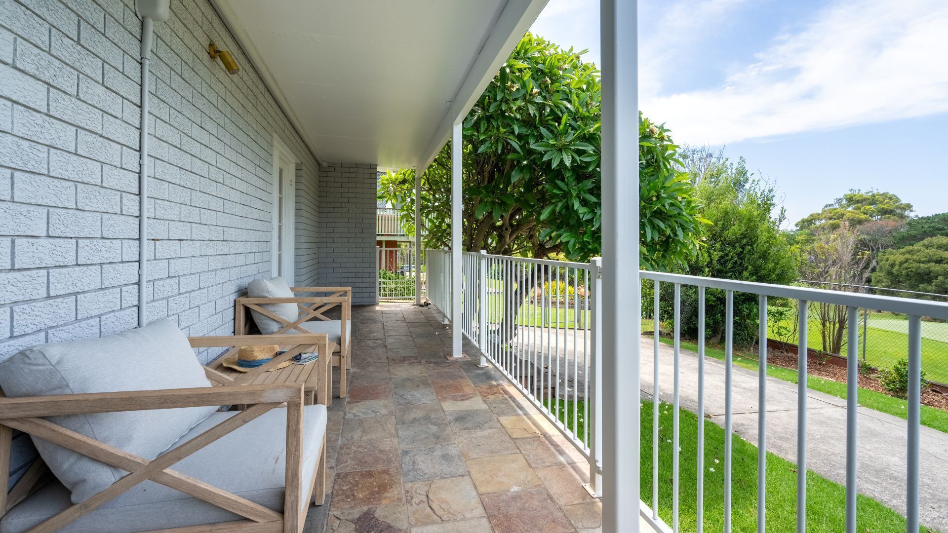 A covered outdoor seating area with stone flooring, white railings, and a view of a green landscape.