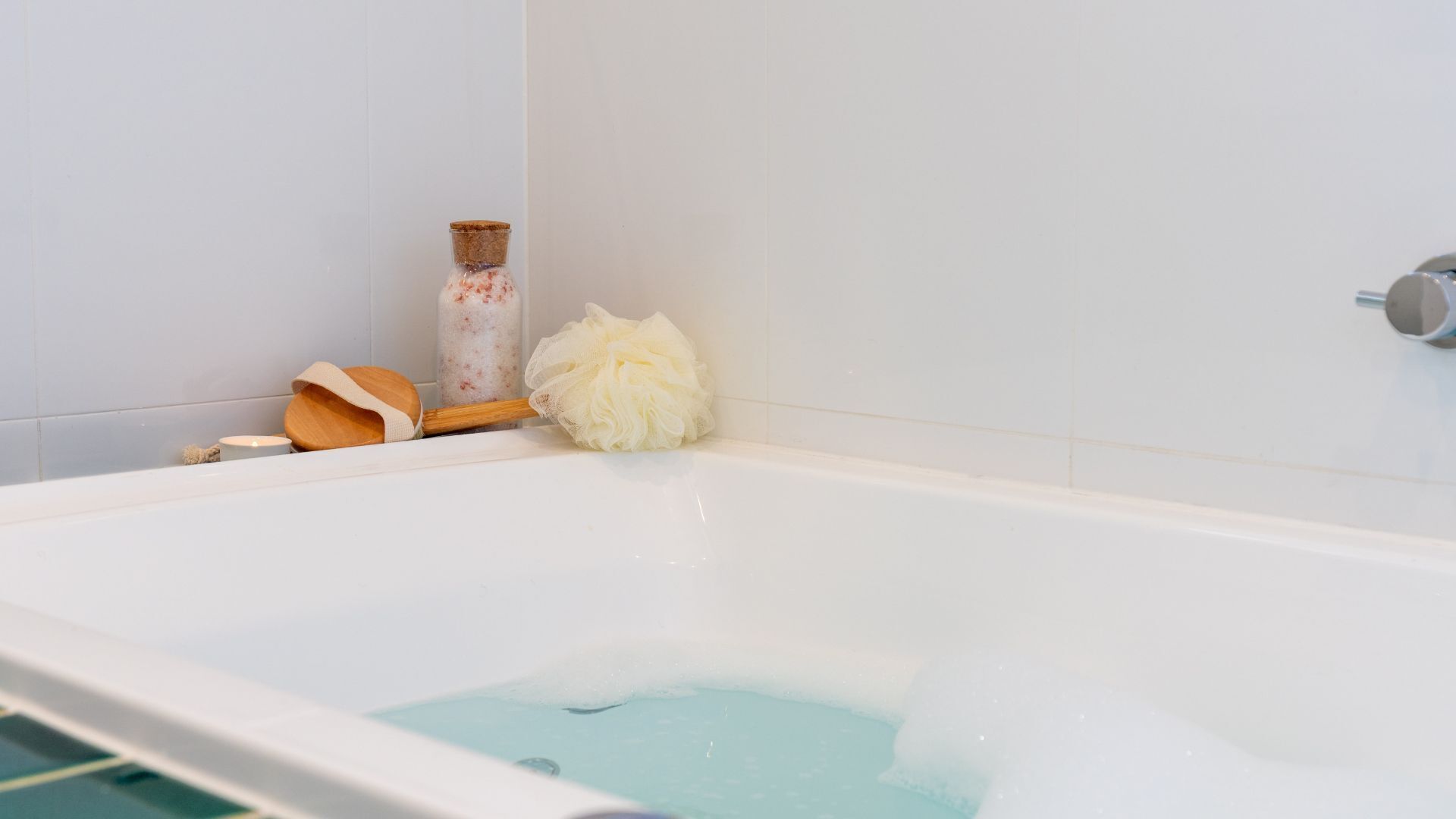 A bathtub with a wooden loofah and a bottle of bath salts.