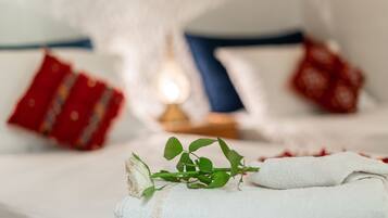 A neatly made bed with a white towel, a rose, and red pillows.
