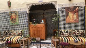 Un interior tradicional marroquí con un mostrador de recepción de madera, baldosas estampadas y cojines coloridos.