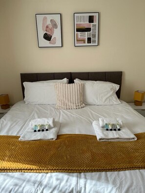 A neatly made bed with white linens, a brown headboard, and two framed artworks above it. - Lovely 2-bed Apartment in Stroud (Stroud)