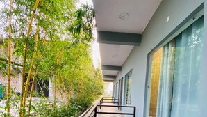 A corridor with patterned flooring, a metal railing, and a row of windows with curtains. - New Corbett Hotel and Resort (Ramnagar)