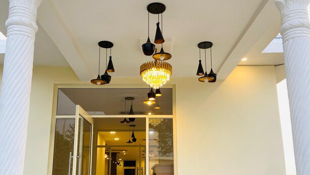 A building entrance with a glass door, multiple hanging lights, and white columns. - New Corbett Hotel and Resort (Ramnagar)