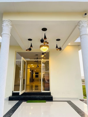 A building entrance with a glass door, multiple hanging lights, and white columns. - New Corbett Hotel and Resort (Ramnagar)