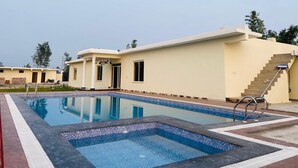 A swimming pool with tiled edges, a staircase leading to a building, and a clear sky. - New Corbett Hotel and Resort (Ramnagar)