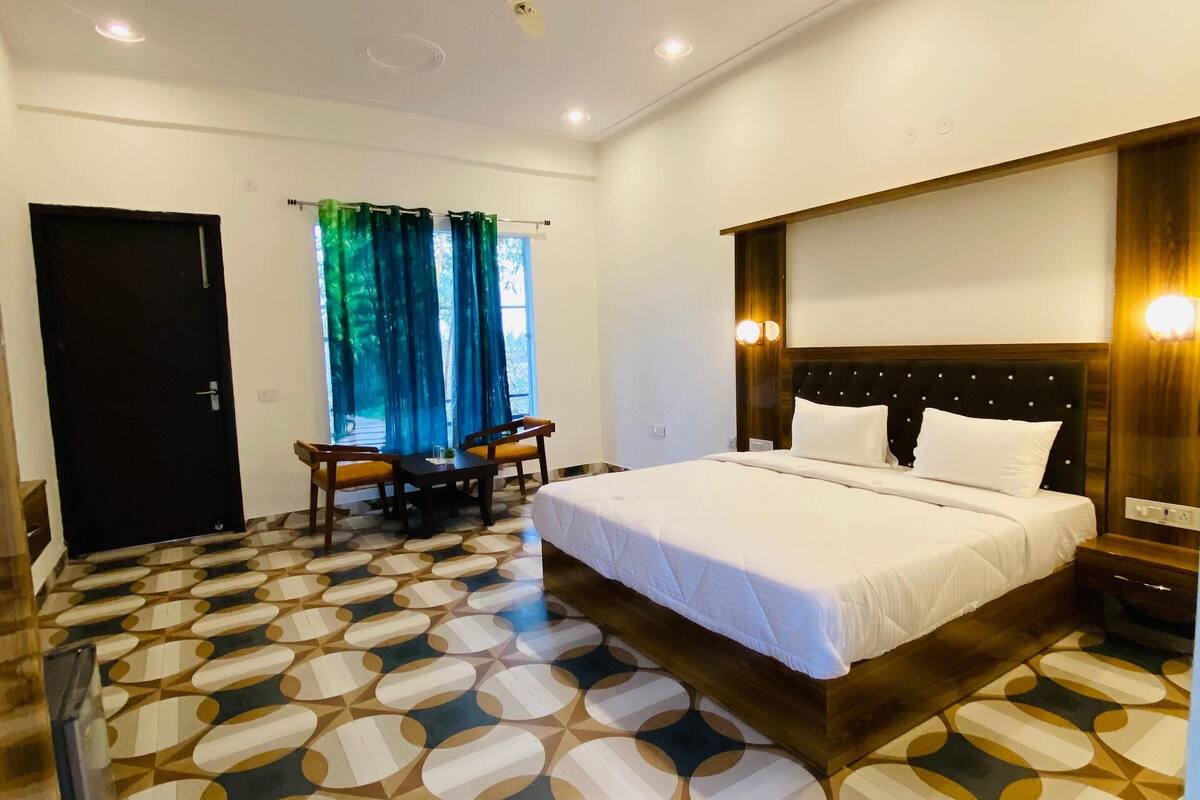 A hotel room with a bed, a desk, a chair, a ceiling fan, and a patterned floor.