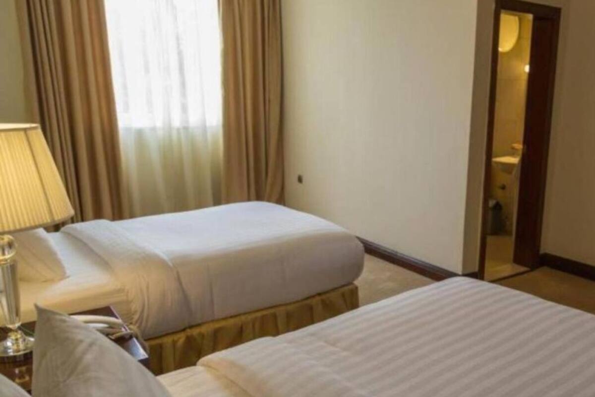 A hotel room with two beds, a lamp, and a door leading to a bathroom.