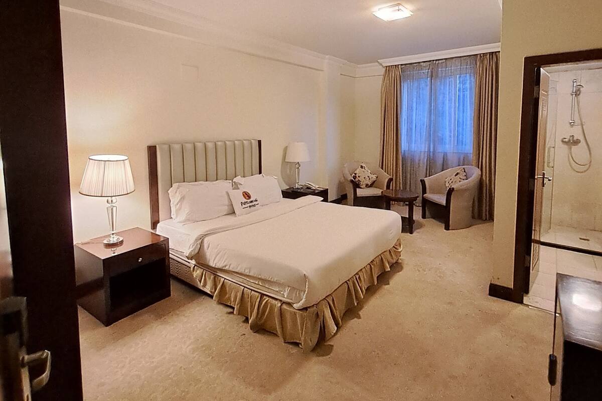 A hotel room with a large bed, two bedside tables, a chair, a desk, and a shower area.