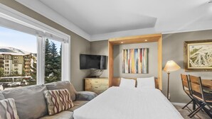 A modern hotel room with a large bed, a sofa, a TV, and a painting. - Tl212 Telemark Lodge Condo by RedAwning (Copper Mountain)
