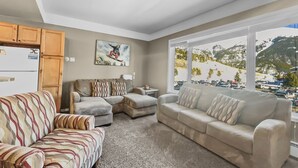 A living room with a sectional sofa, a loveseat, and a couch. There is a painting on the wall and a window with a view of a parking lot and mountains. - Tl212 Telemark Lodge Condo by RedAwning (Copper Mountain)