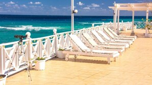 Une terrasse avec des chaises longues blanches et un appareil photo posé sur un trépied, d’où l’on peut admirer une mer turquoise.