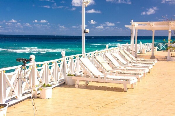 A deck with white lounge chairs and a camera on a tripod, overlooking a turquoise sea.