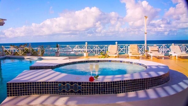 Un espace piscine doté d’un jacuzzi, de chaises longues et offrant une vue sur l’océan.