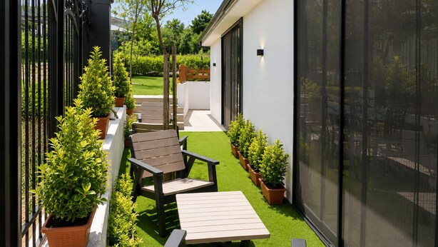 A modern outdoor patio with a wooden table and chairs, surrounded by potted plants and a white building with large windows.