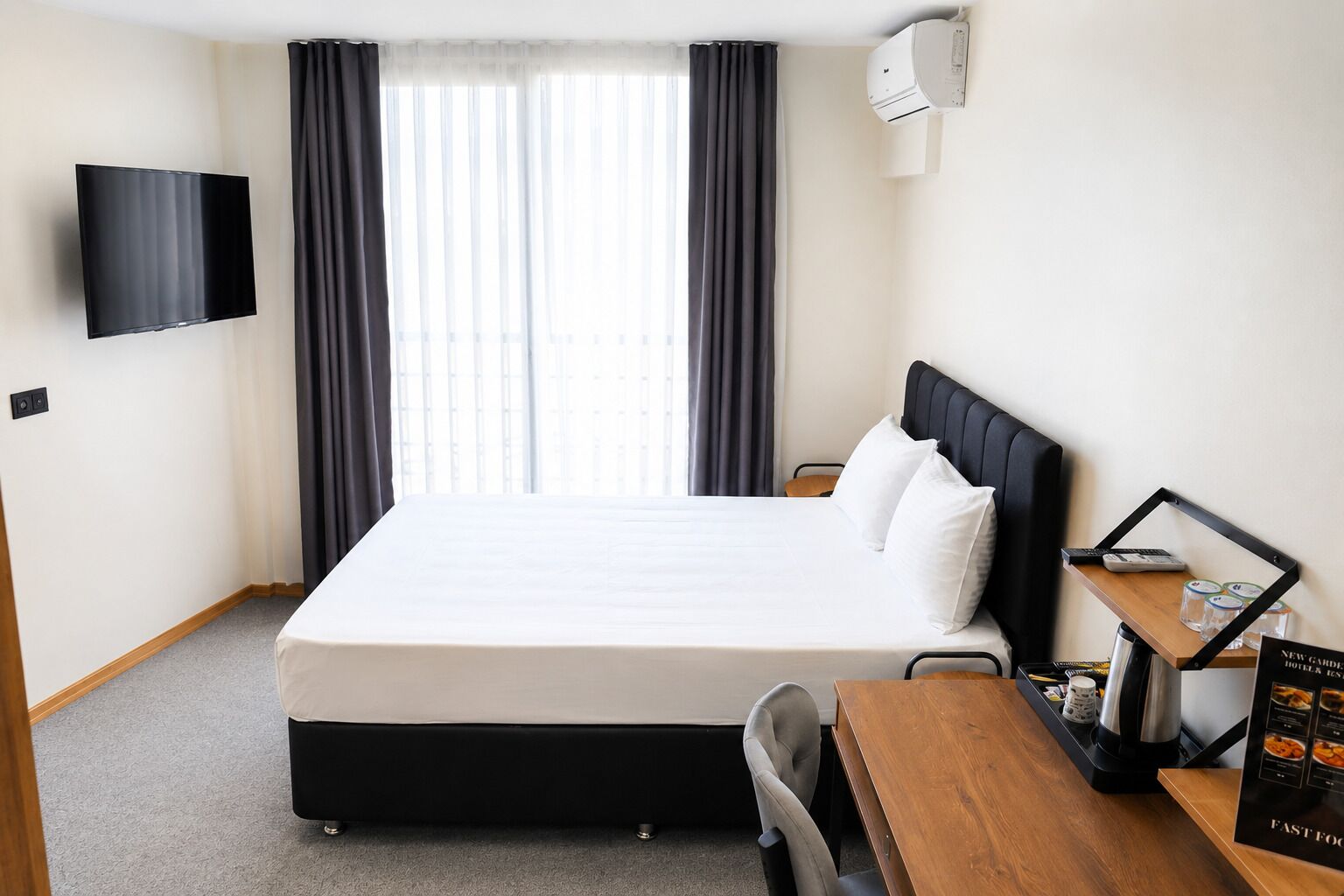 Habitación de hotel con cama, escritorio con cafetera, televisor y ventana con cortinas.