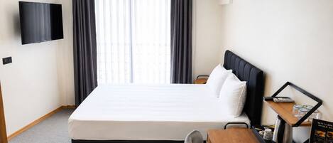 Habitación de hotel con cama, escritorio con cafetera, televisor y ventana con cortinas.