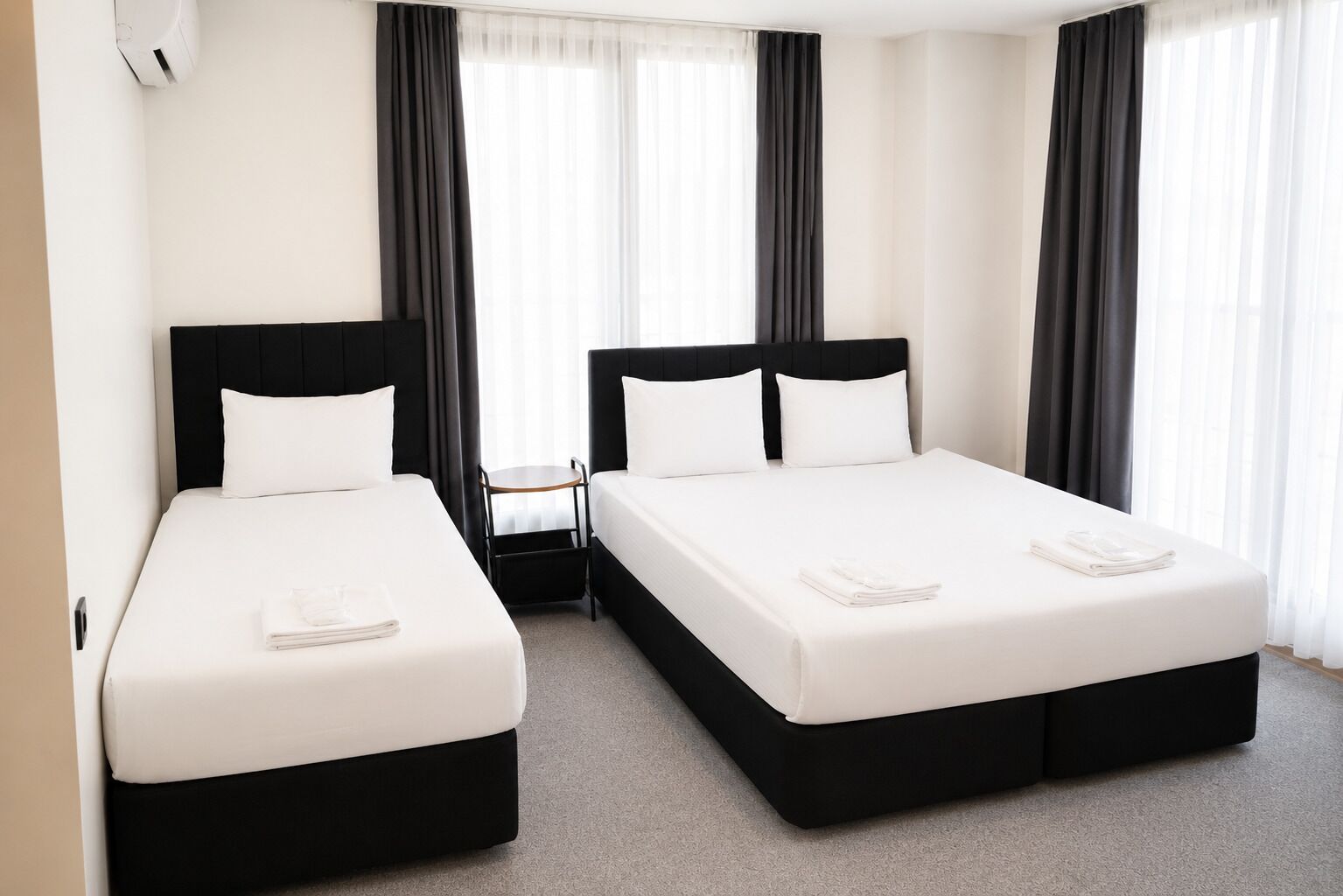 A hotel room with two beds, a small table, and a window with curtains.