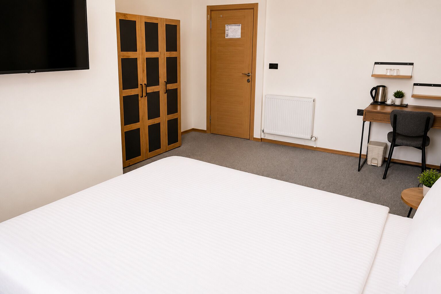 A bedroom with a bed, a desk with a chair, a radiator, and a wardrobe with glass doors.