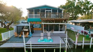 A waterfront property with a deck, outdoor seating, and a sign that reads "30 MORE OF WHAT MAKES YOU HAPPY." - River home with huge arcade, hot tub, kayaks, mini golf course, 80in TV (Spring Hill)