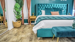 A bedroom with a teal upholstered headboard, a white bedspread, and a matching bench. - River home with huge arcade, hot tub, kayaks, mini golf course, 80in TV (Spring Hill)