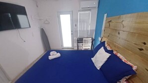 Una habitación con una cama, un televisor en la pared, una puerta y una ventana con persianas.
