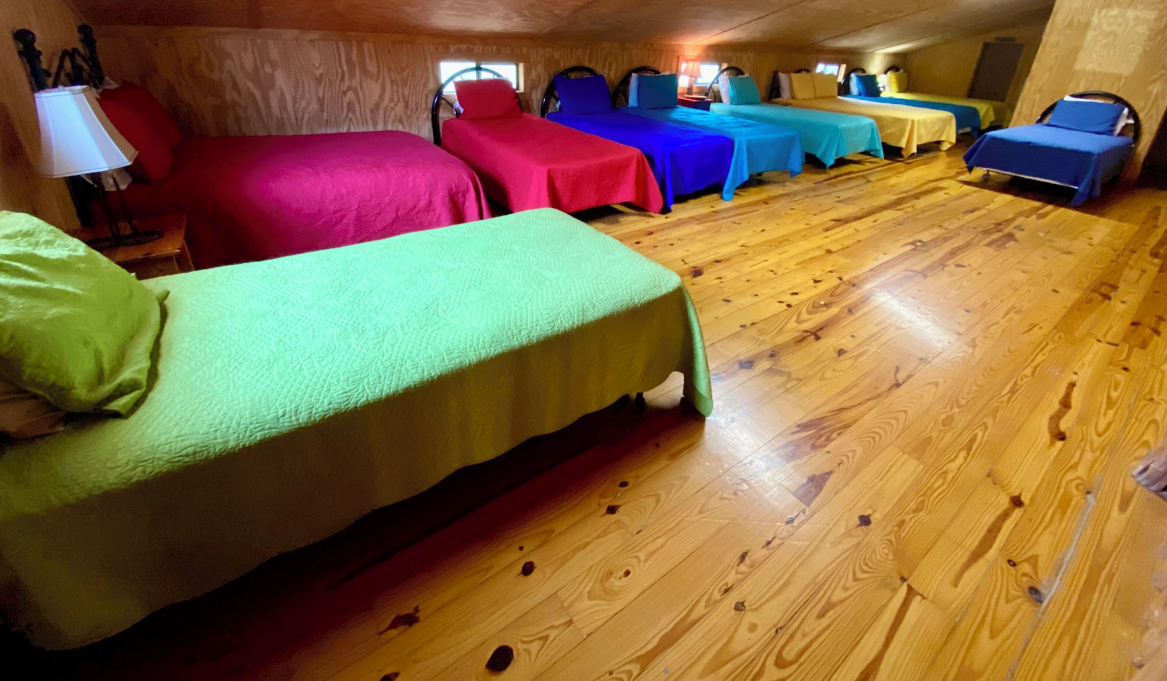 Quarto com piso de madeira e várias camas com roupa de cama colorida.