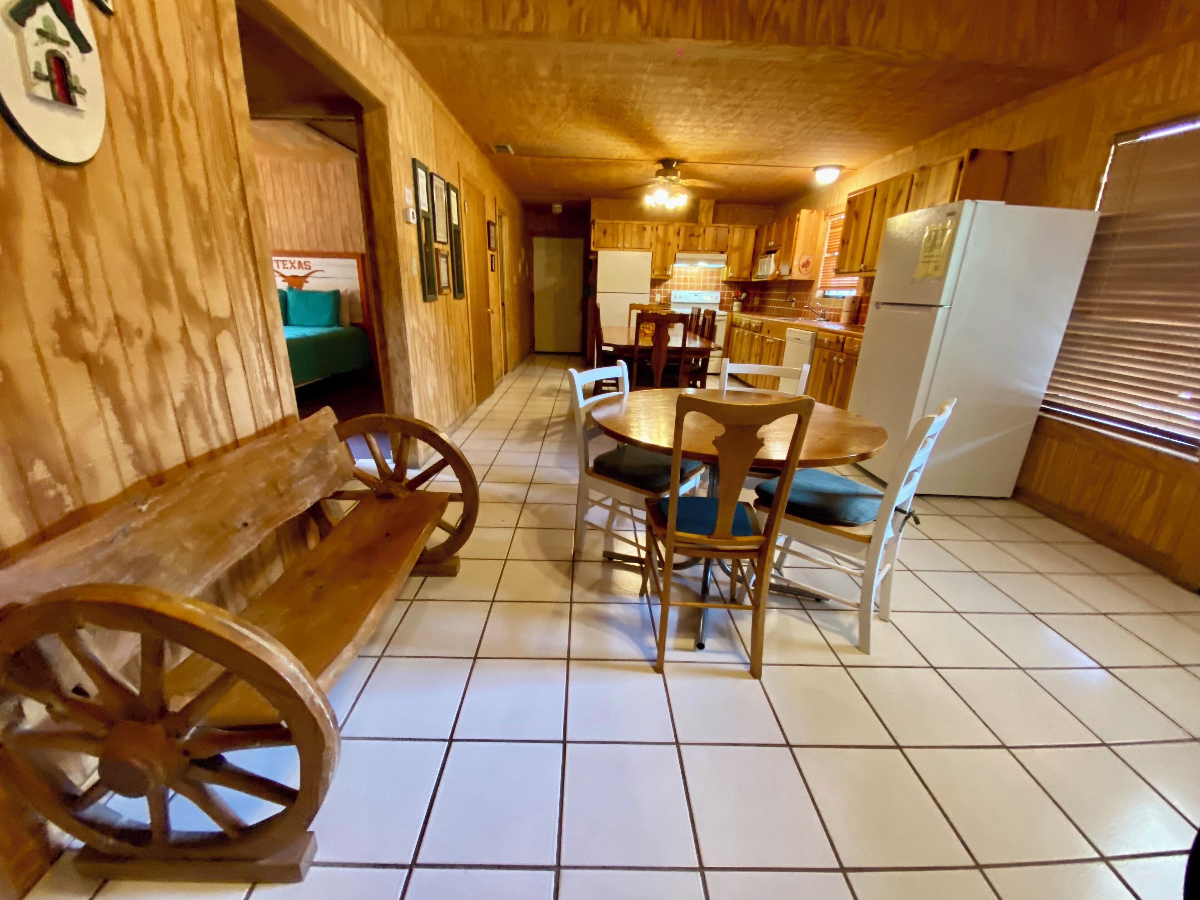 A wooden interior with a dining table, chairs, a bench, and a refrigerator.