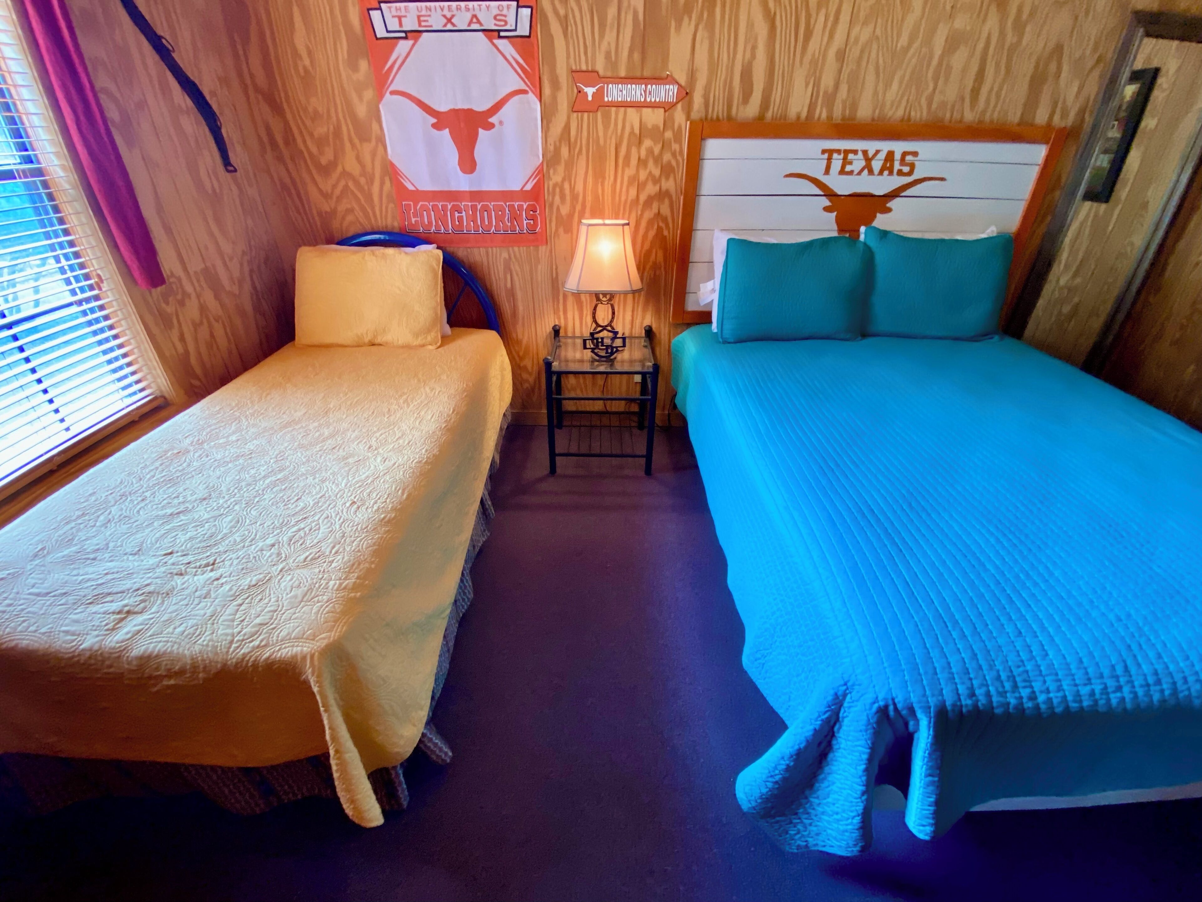 A room with two beds, a nightstand, a lamp, and Texas-themed decorations.