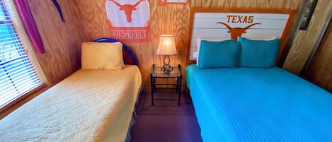 A room with two beds, a nightstand, a lamp, and Texas-themed decorations.