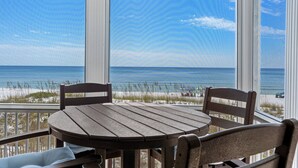 Une table et des chaises en bois sur un balcon donnant sur la plage et l’océan.