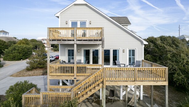 A two-story house with a wooden deck and a staircase leading to the upper floor.