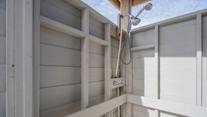 A corner of a room with a shower enclosure, wooden beams, and a white exterior wall.