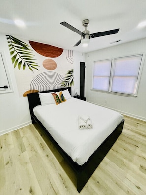 A modern bedroom with a bed, ceiling fan, and windows.