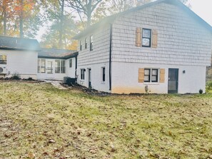 A two-story house with a white exterior and a large front yard. - Vibrant 4BR Split-Level Home Near PTI Airport (Greensboro)