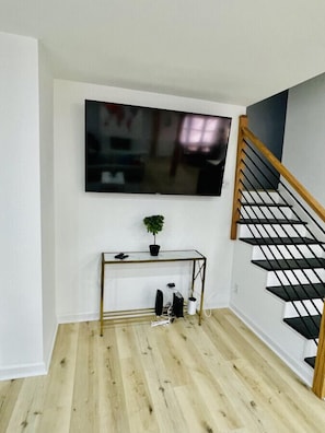 A room with a flat-screen TV mounted on the wall, a small table with a plant, and a staircase with wooden railings.