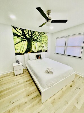 A bedroom with a bed, a nightstand, a ceiling fan, and a large forest-themed tapestry on the wall. - Vibrant 4BR Split-Level Home Near PTI Airport (Greensboro)