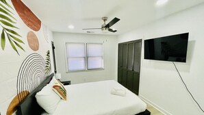 A bedroom with a bed, a ceiling fan, a TV mounted on the wall, and a window with blinds.